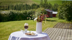 Taula amb postre, un got de cafè i un ram de flors sobre un pont de fusta amb una vista panoràmica d'una granja i un edifici vermell al fons.