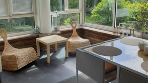 Una sala de estar con ventanales amplios, muebles de mimbre y una mesa de vidrio.