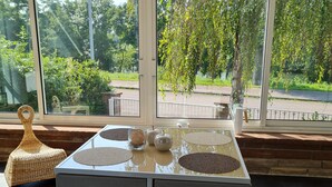 Una mesa con una silla de mimbre, vistas al verdor exterior y un cielo despejado.