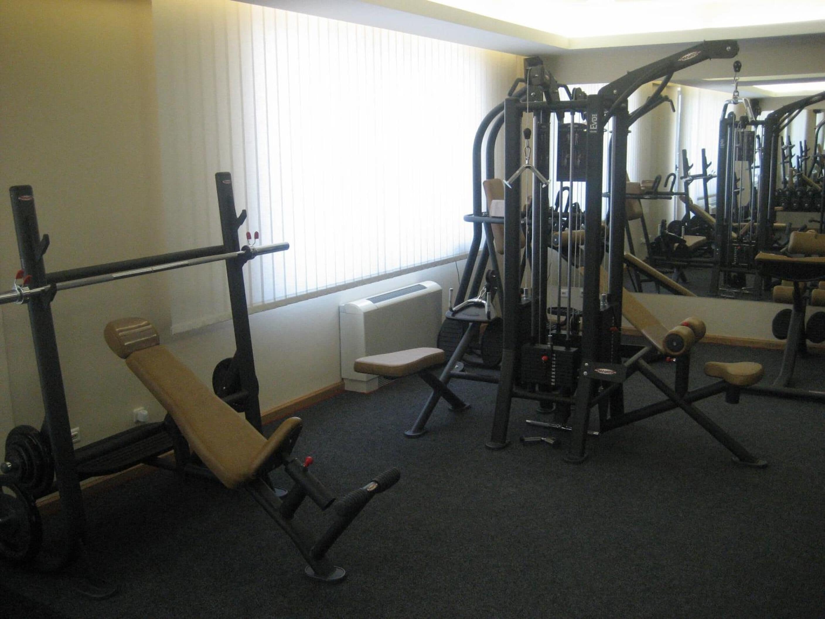 Un gimnasio con diferentes equipos de ejercicio, una banca y un radiador cerca de la ventana.