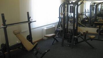 Un gimnasio con diferentes equipos de ejercicio, una banca y un radiador cerca de la ventana.