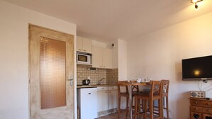 Cocina compacta con microondas, pileta y comedor con sillas. Hay un televisor y una radio en la pared.