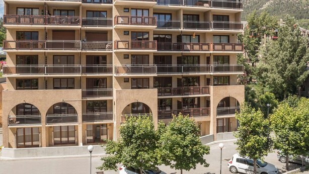 Un hotel de varios pisos con balcones, ventanas arqueadas y montañas al fondo.