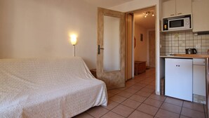 Una habitación pequeña y limpia con una cama, un rincón de cocina y una puerta que da a otra habitación.