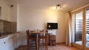 Una cocina compacta con mesa, sillas, televisor y un mueble pequeño.