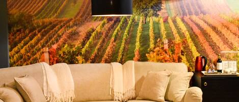 A living room with a beige sofa, a round coffee table, and a wall mural of vineyards.