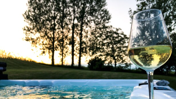 A glass of white wine on a table by a hot tub with a view of trees and a sunset. - Sydkustens at Pillehill (Skivarp)
