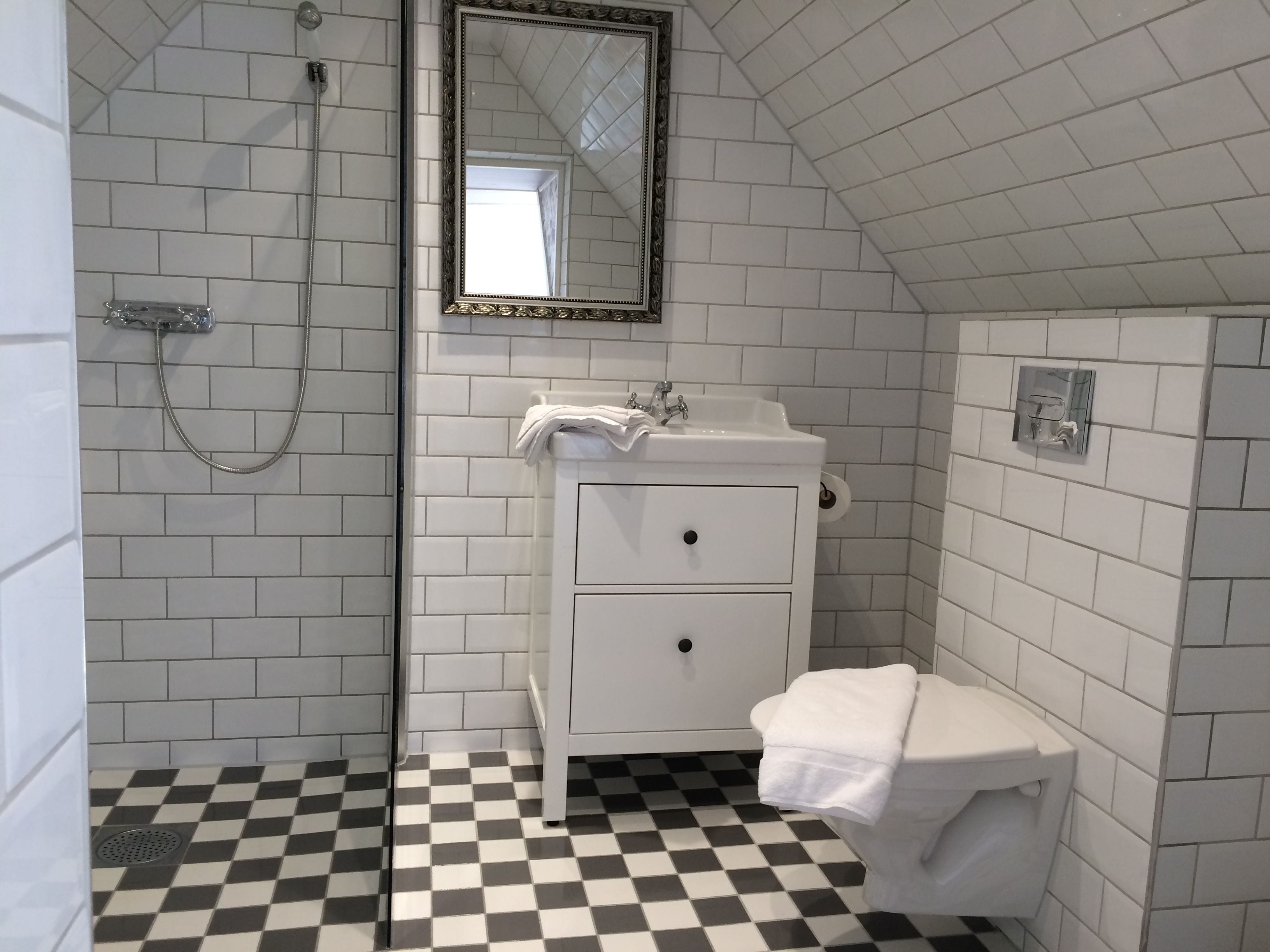 A bathroom with white tiled walls, a checkered floor, a white sink with a mirror above it, and a shower with a glass door.