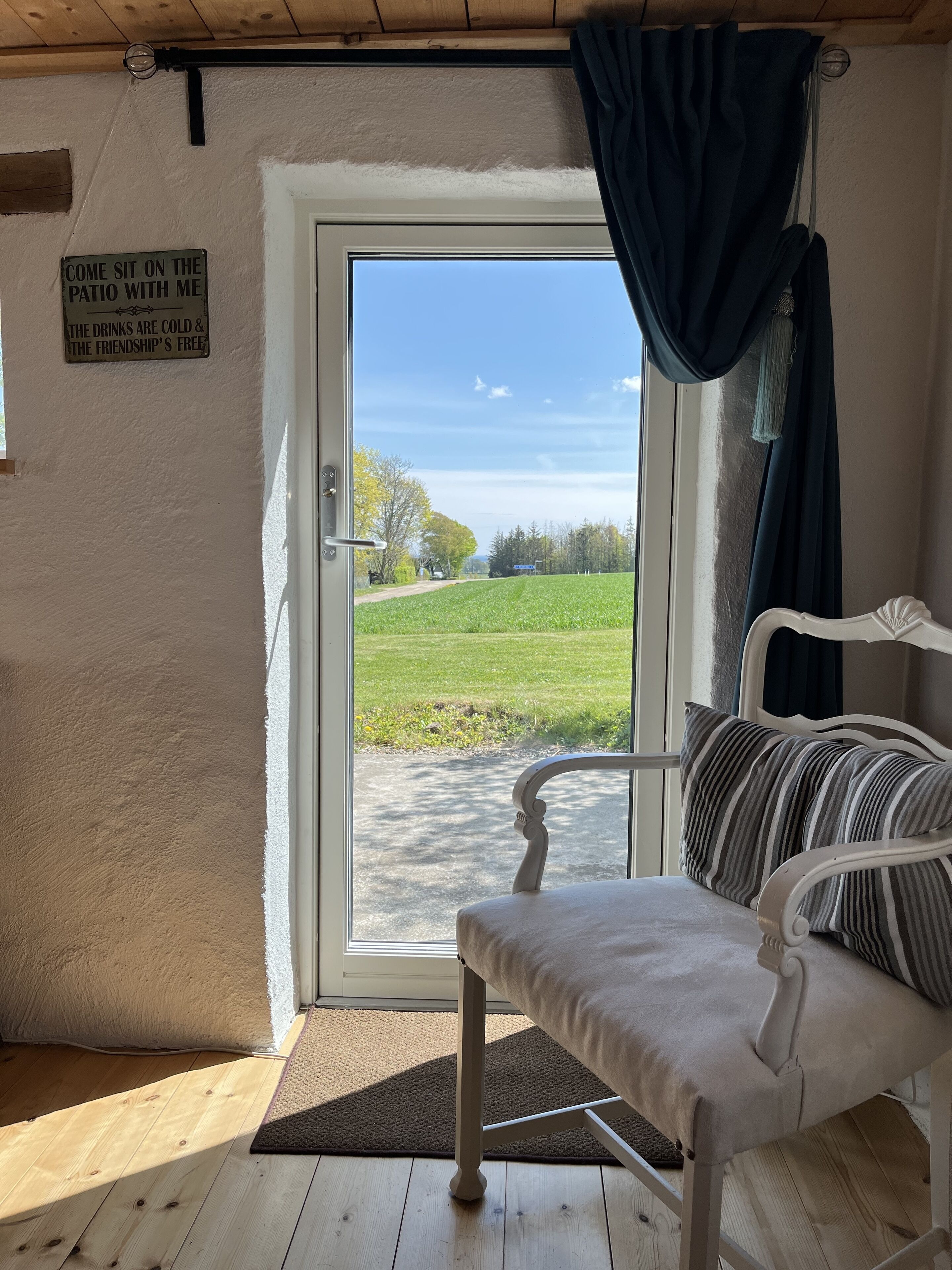 Een gezellige kamer met een witte bank en een bord dat gasten uitnodigt voor het terras.