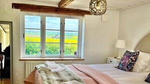 A bedroom with a large bed, a view of the countryside through a window, and a wooden ceiling. - Sydkustens at Pillehill (Skivarp)