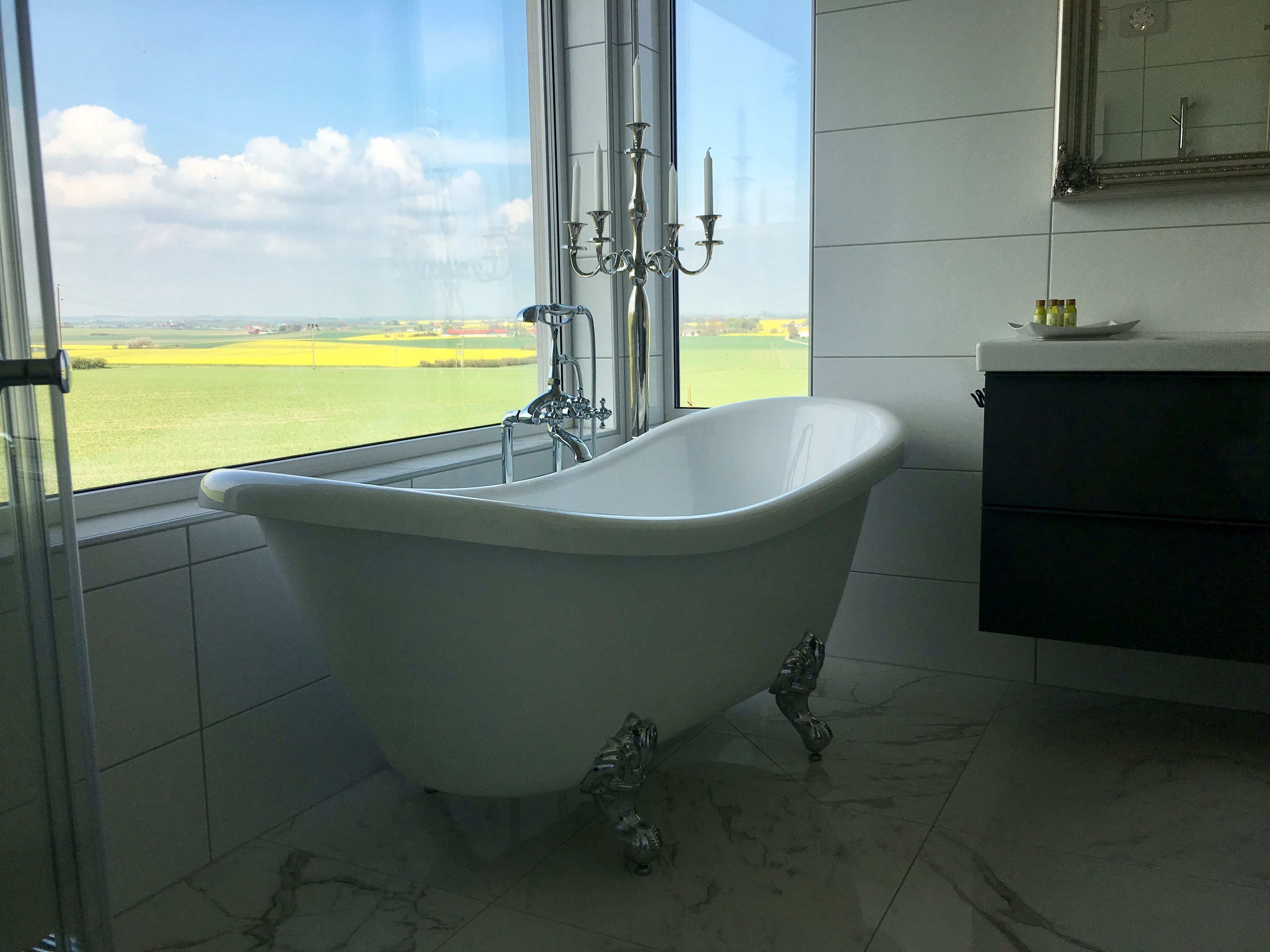 A bathroom with a freestanding bathtub, a large window with a view of a green field, and a modern vanity with a mirror.