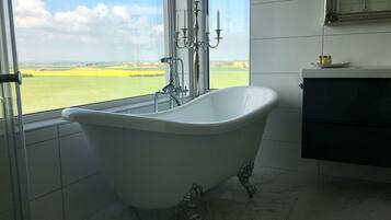 A bathroom with a freestanding bathtub, a large window with a view of a green field, and a modern vanity with a mirror.
