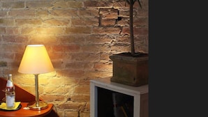 A room with a brick wall, a table with a lamp, a potted plant, and a television set. - Hotel Berliner Hof Dallgow (Dallgow-Doeberitz)