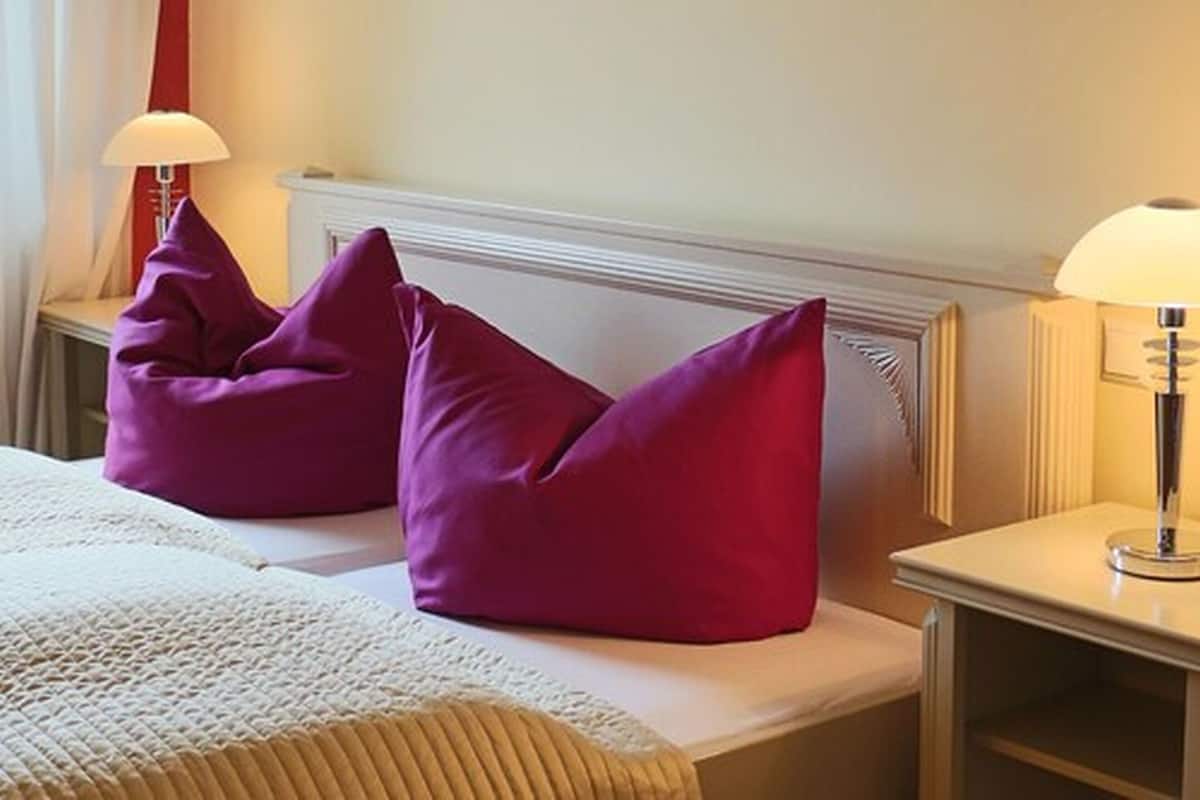 A neatly made bed with two pillows, a bedside lamp, and a nightstand.