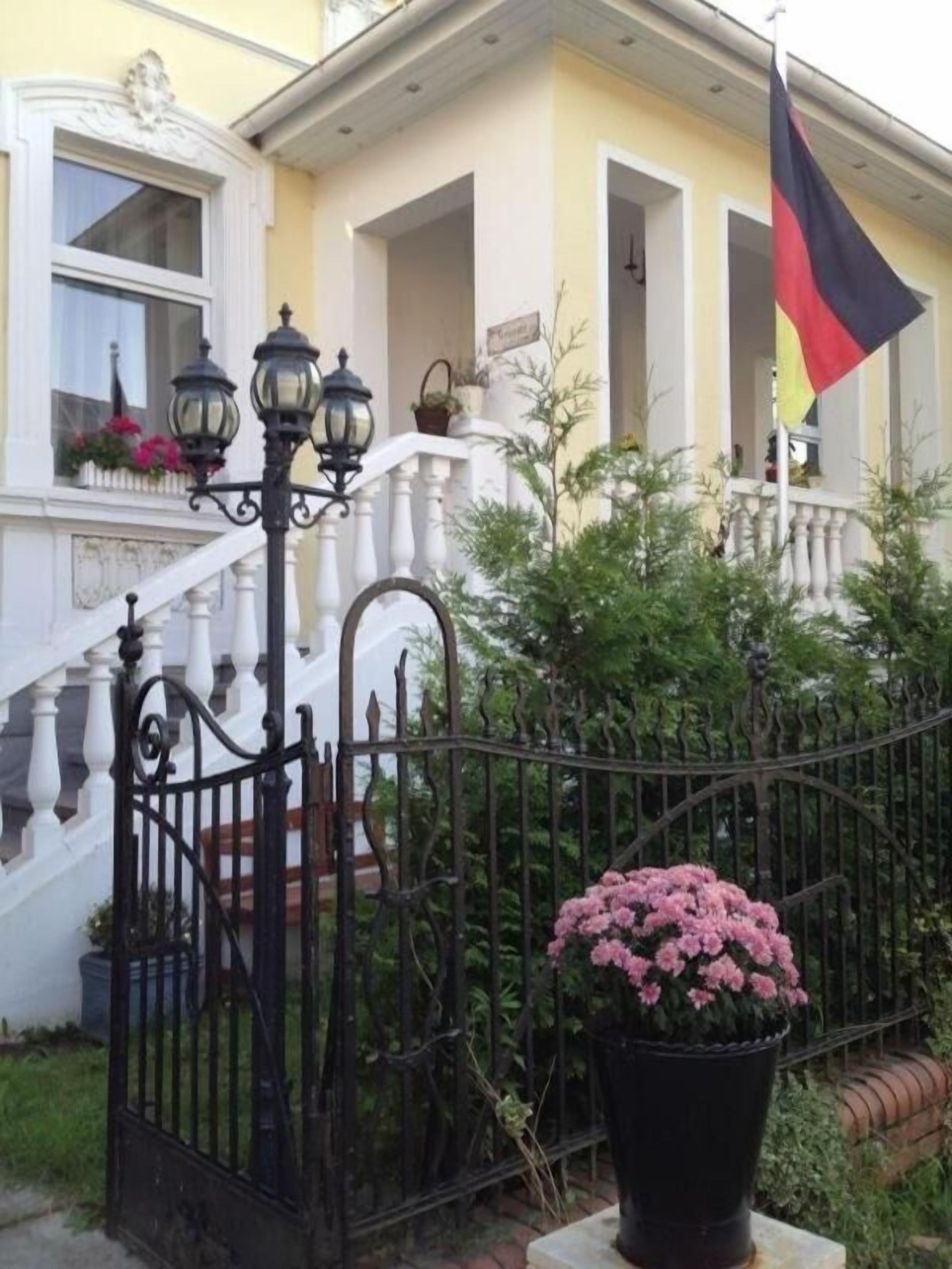 A yellow building with a white staircase, a black metal fence, and a flag.