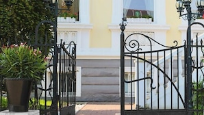 A gated entrance with a wrought iron gate, a potted plant, and a building with white trim and a yellow facade. - Hotel Berliner Hof Dallgow (Dallgow-Doeberitz)