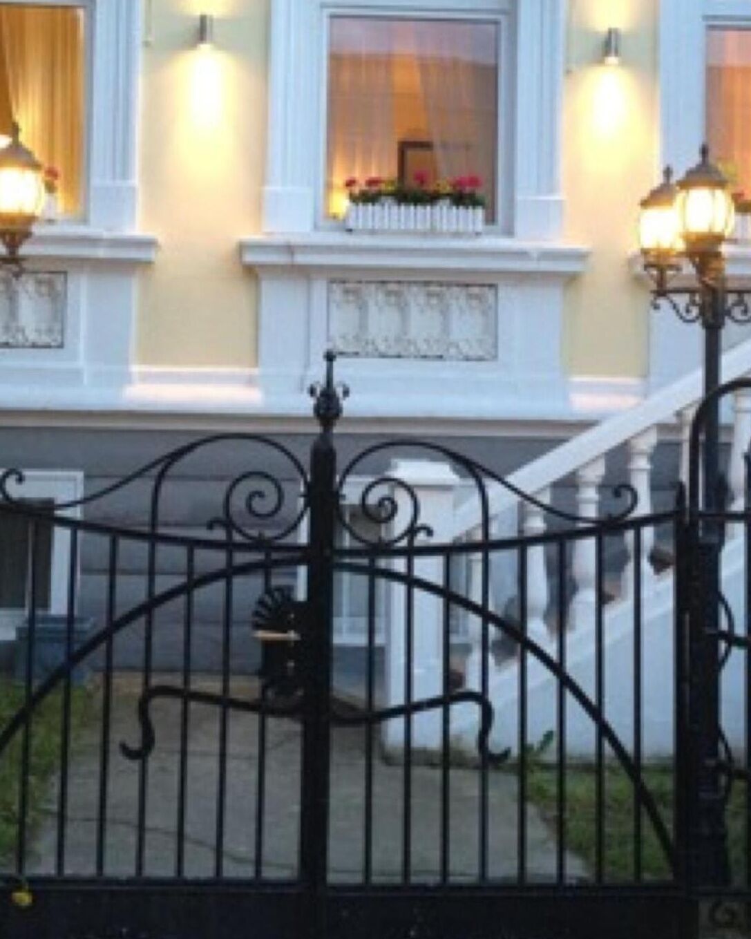 A building with a white facade, a black wrought iron gate, and a staircase leading to the entrance.