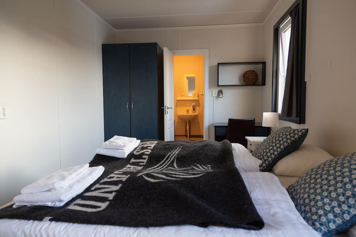 Quarto com cama, guarda-roupa, banheiro visível por uma porta aberta e mesa de cabeceira com abajur.