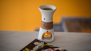 A candle in a white holder on a table with a comic book titled "Superman" in front of it.