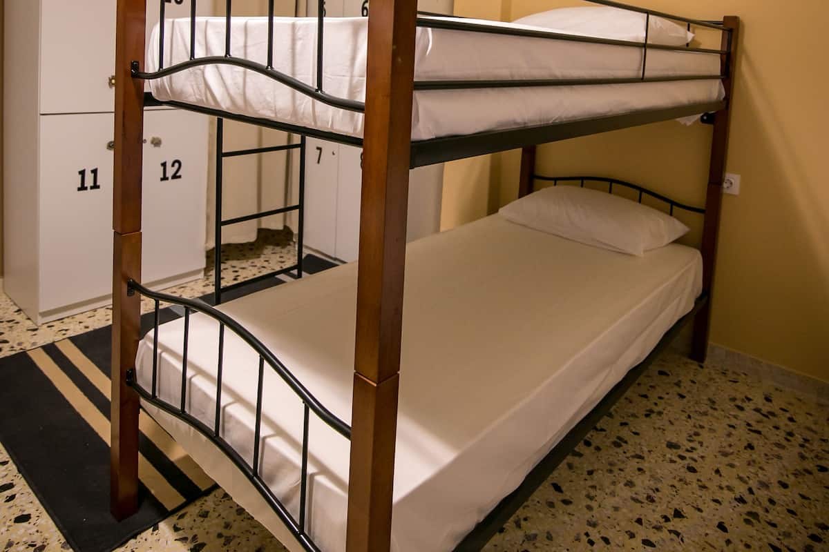 A bunk bed with a wooden frame and metal railings, a white mattress, and a black and white striped rug.