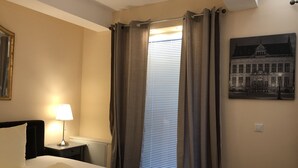 A hotel room with a bed, a nightstand, a lamp, a window with curtains, and a wall-mounted picture. - Gatow 183 (Berlin)
