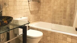 Un bagno con un water, un lavandino in vetro e una vasca.