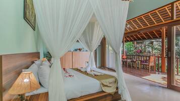 A four-poster canopy bed with white bedding and rose petals, a wooden headboard, and a bedside lamp.