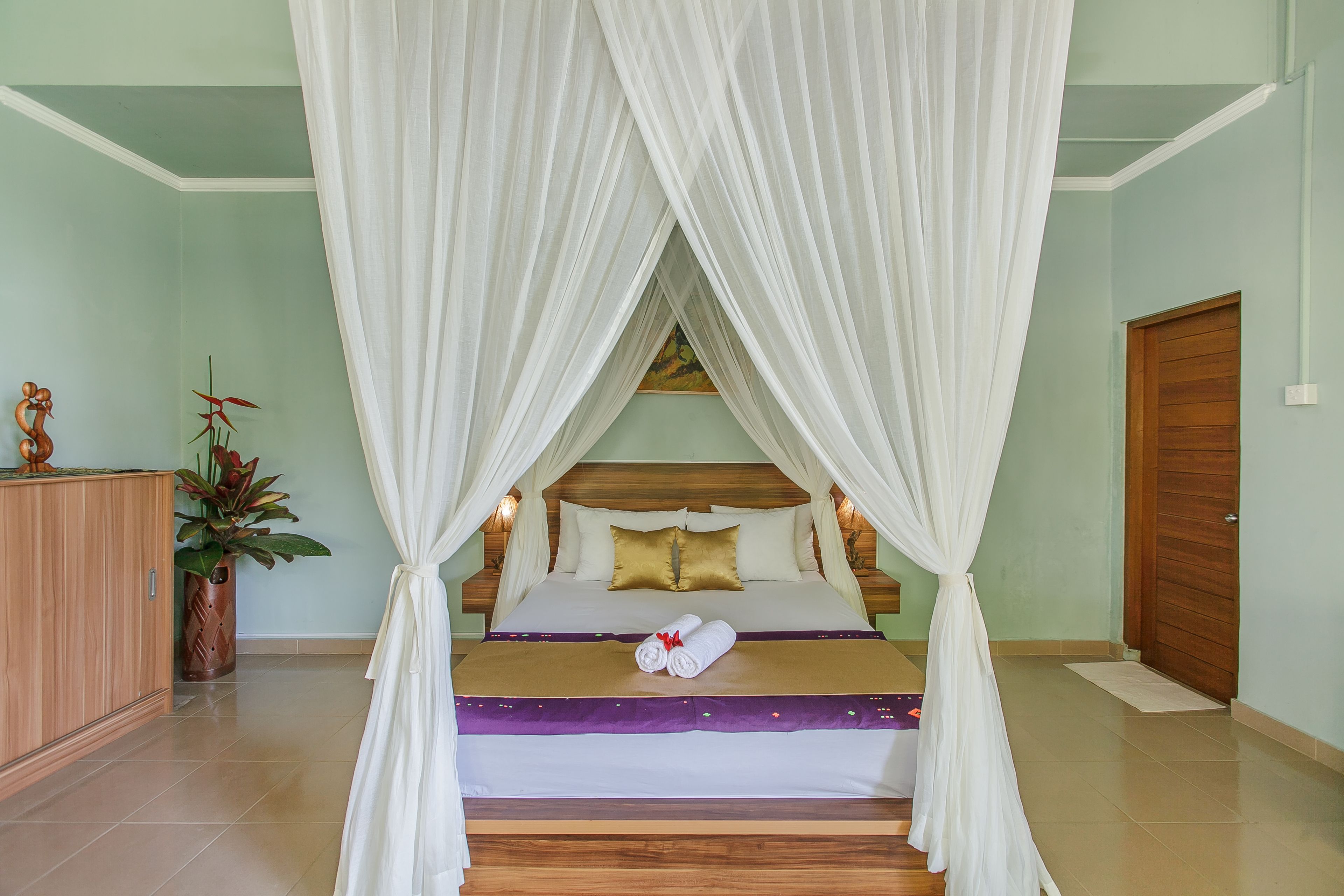 Una cama bien hecha con dosel, un cabecero de madera y un cojín decorativo.