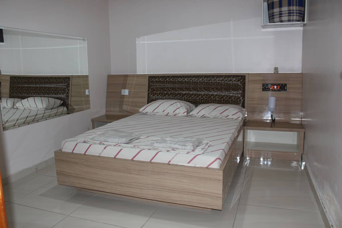 A modern bedroom with a wooden bed, a nightstand, a digital clock, and a mirror.