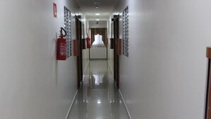 A long, narrow hallway with a shiny floor, doors on both sides, and a fire extinguisher on the left. - Hotel Flert Tatuape (São Paulo)