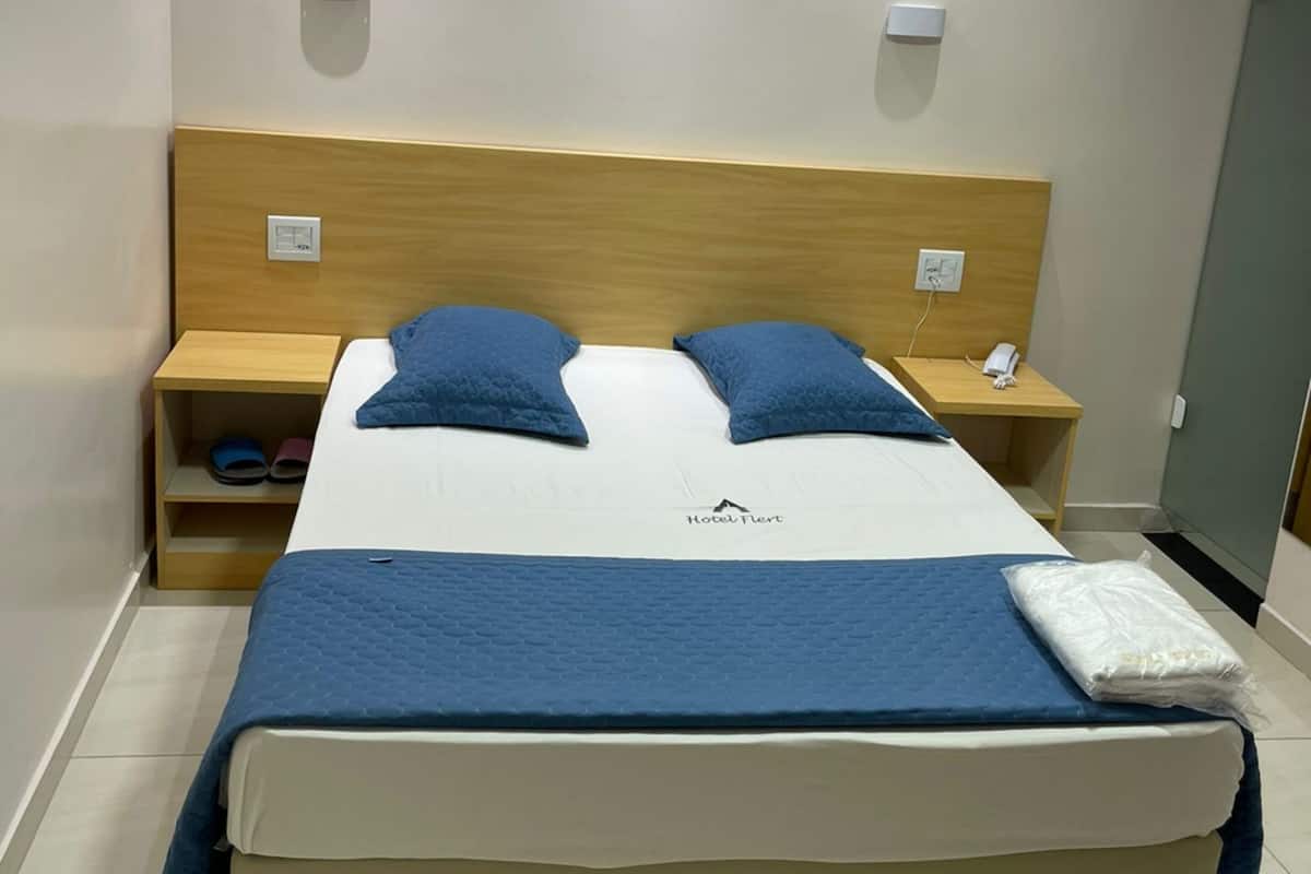 A hotel room with a bed, two bedside tables, a wooden headboard, and a small shelf.