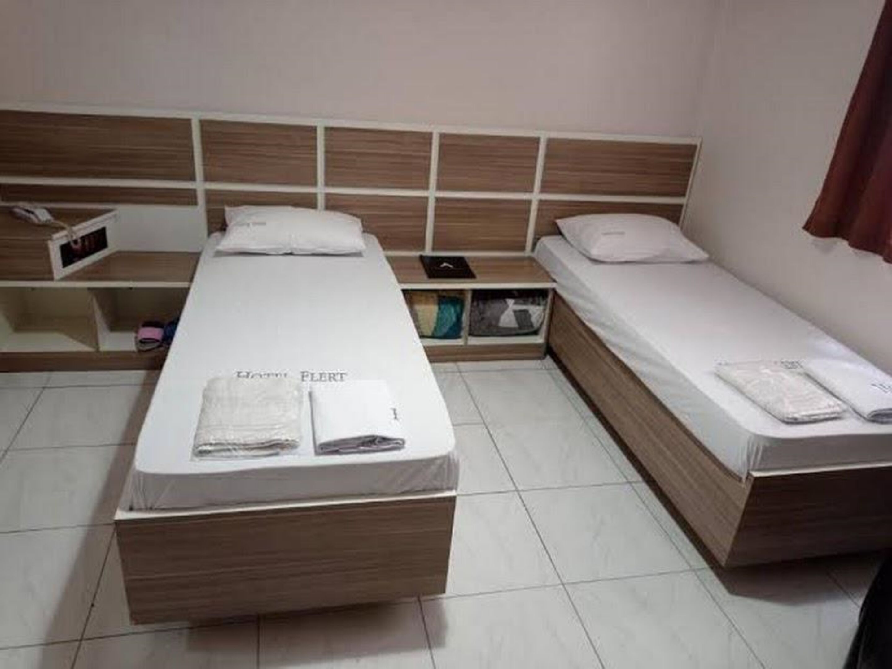 A room with two single beds, a wooden headboard, a small shelf, and a bedside table.