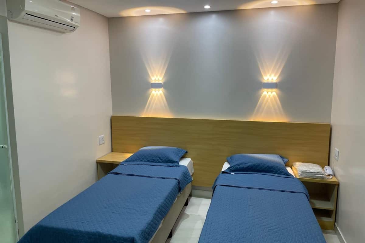 A hotel room with two single beds, a wooden headboard, and wall-mounted lighting.