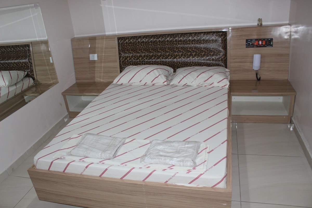 A neatly made bed with a striped bedspread, a headboard with a leopard print design, and a bedside table with a phone.