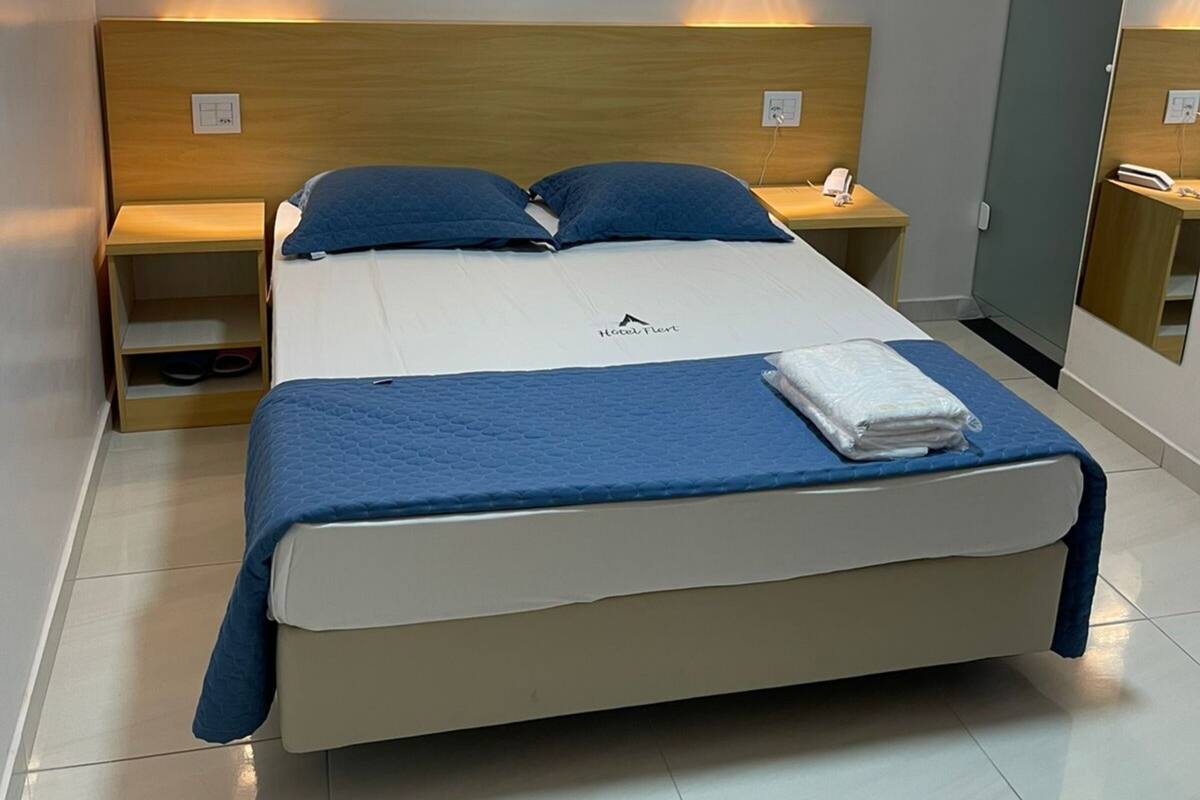 A hotel room with a bed, bedside tables, a nightstand, a mirror, and a wardrobe.