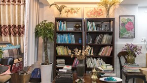 Eine gemütliche Leseecke mit Bücherregal, Schreibmaschine, Blumen in einer Vase und einer Topfpflanze.