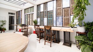 Ein modernes Interieur mit einem langen Holztisch, mehreren Stühlen und einem großen Fenster mit verzierten Fensterläden.