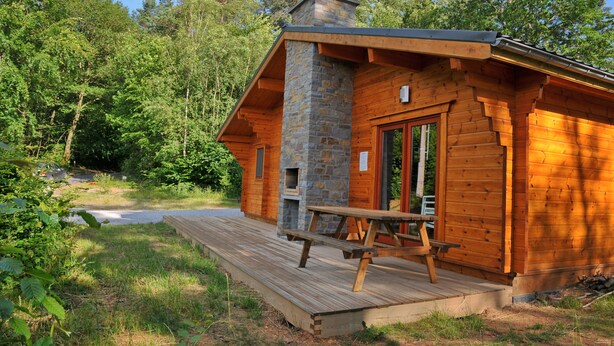 A wooden cabin with a stone chimney, a wooden deck, and a picnic table. - Abri Vert (Viroinval)