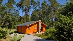 A cabin with a stone chimney, a wooden deck, and a view of a forest. - Abri Vert (Viroinval)