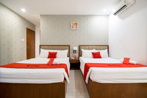 Une chambre d’hôtel avec deux lits, chacun recouvert d’une couverture rouge et doté de draps blancs. Il y a une table de chevet avec une lampe entre les deux lits, et un climatiseur fixé au mur.