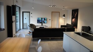 A modern kitchen with a dining area, a sofa, and a TV. - Ard'cube (Somme-Leuze)