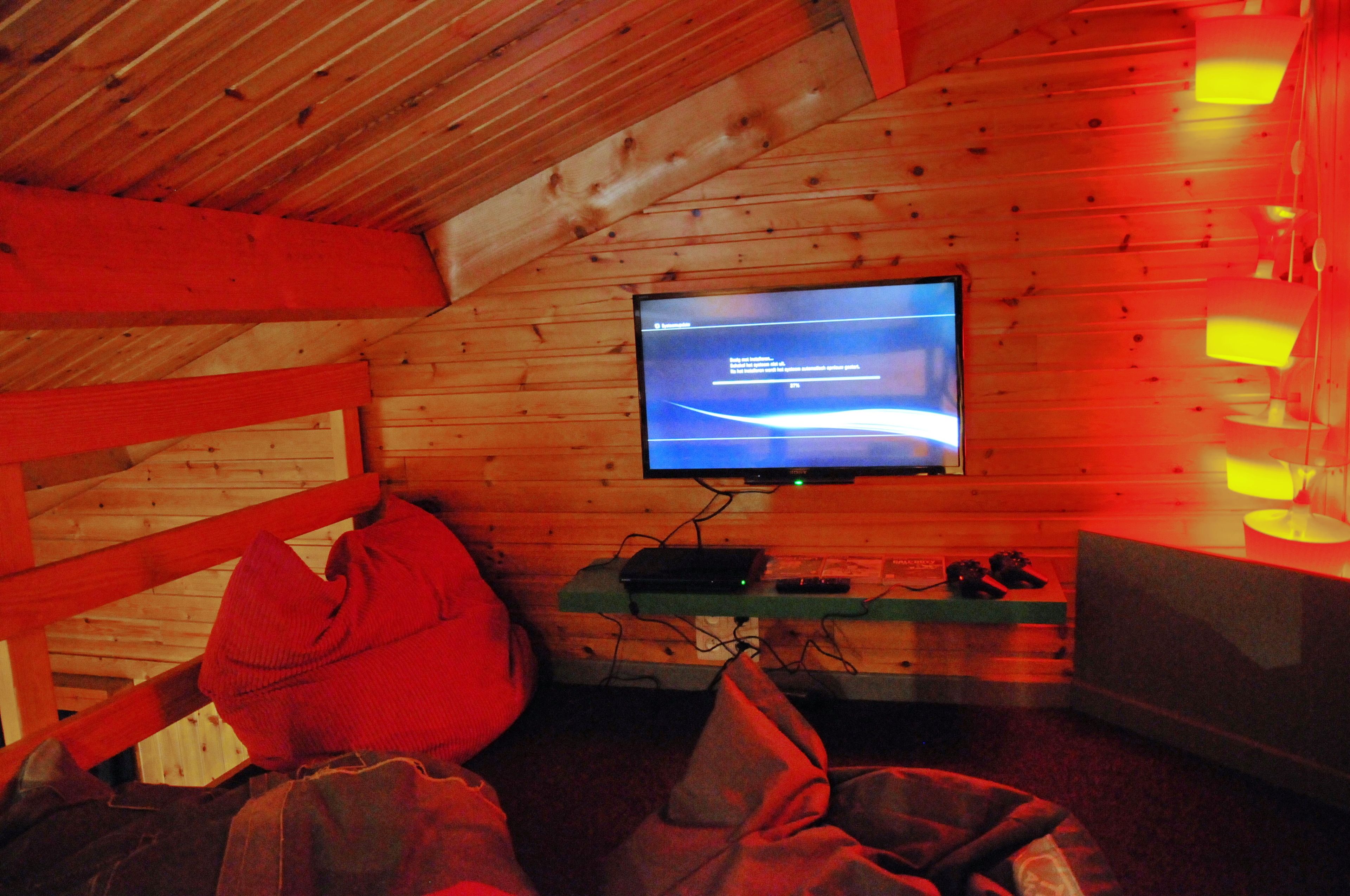 Ein gemütliches Zimmer mit Fernseher an einer Holzwand, einem kleinen Tisch mit Fernbedienung und einer Bank.