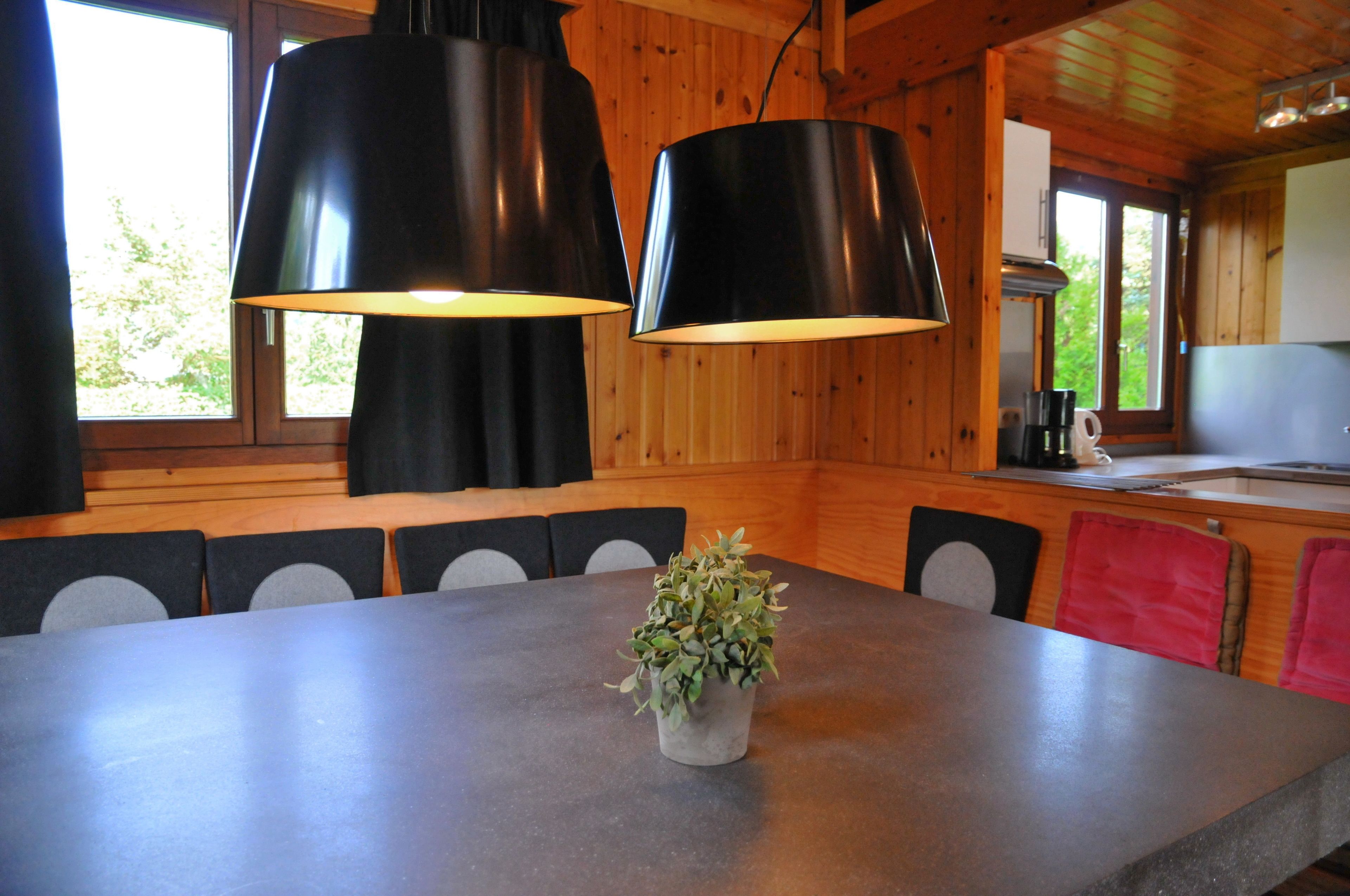A wooden interior with a dining table, chairs, and pendant lights.