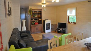 A cozy living room with a sofa, chairs, a television, and a kitchen area with cabinets and a refrigerator. - Au Fil de l'Eau (Durbuy)