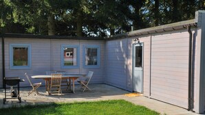 A small, single-story building with a patio area featuring a table and chairs, a grill, and a door. - Au Fil de l'Eau (Durbuy)