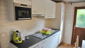 A compact kitchen with white cabinets, a black countertop, a built-in oven, a coffee maker, and a kettle. - Au Fil de l'Eau (Durbuy)