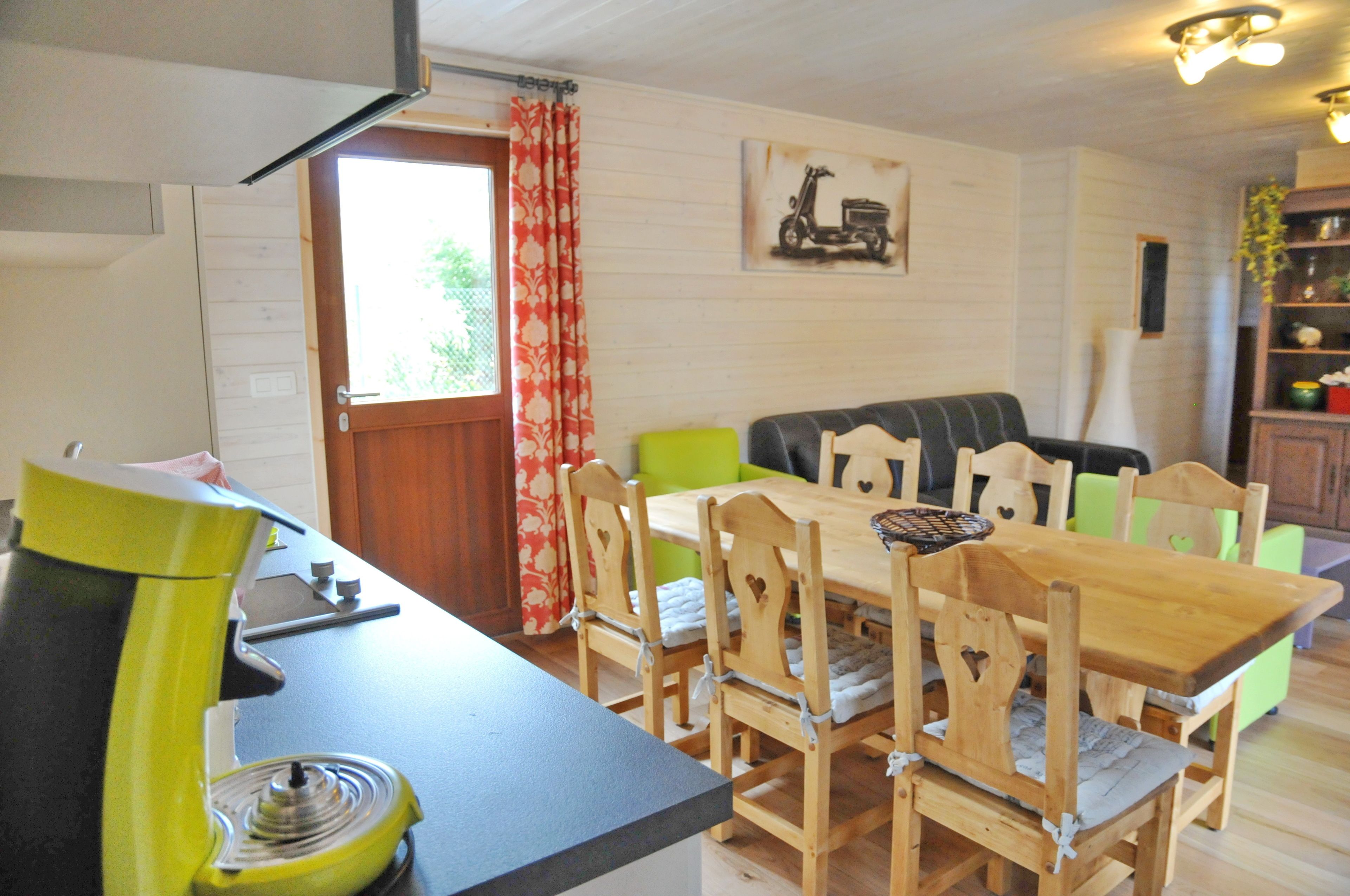A dining area with a wooden table and chairs, a yellow appliance, and a window with red curtains.