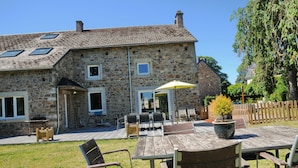 A stone building with a patio area featuring outdoor furniture and a table. - Au Phil du Temps (Erezee)