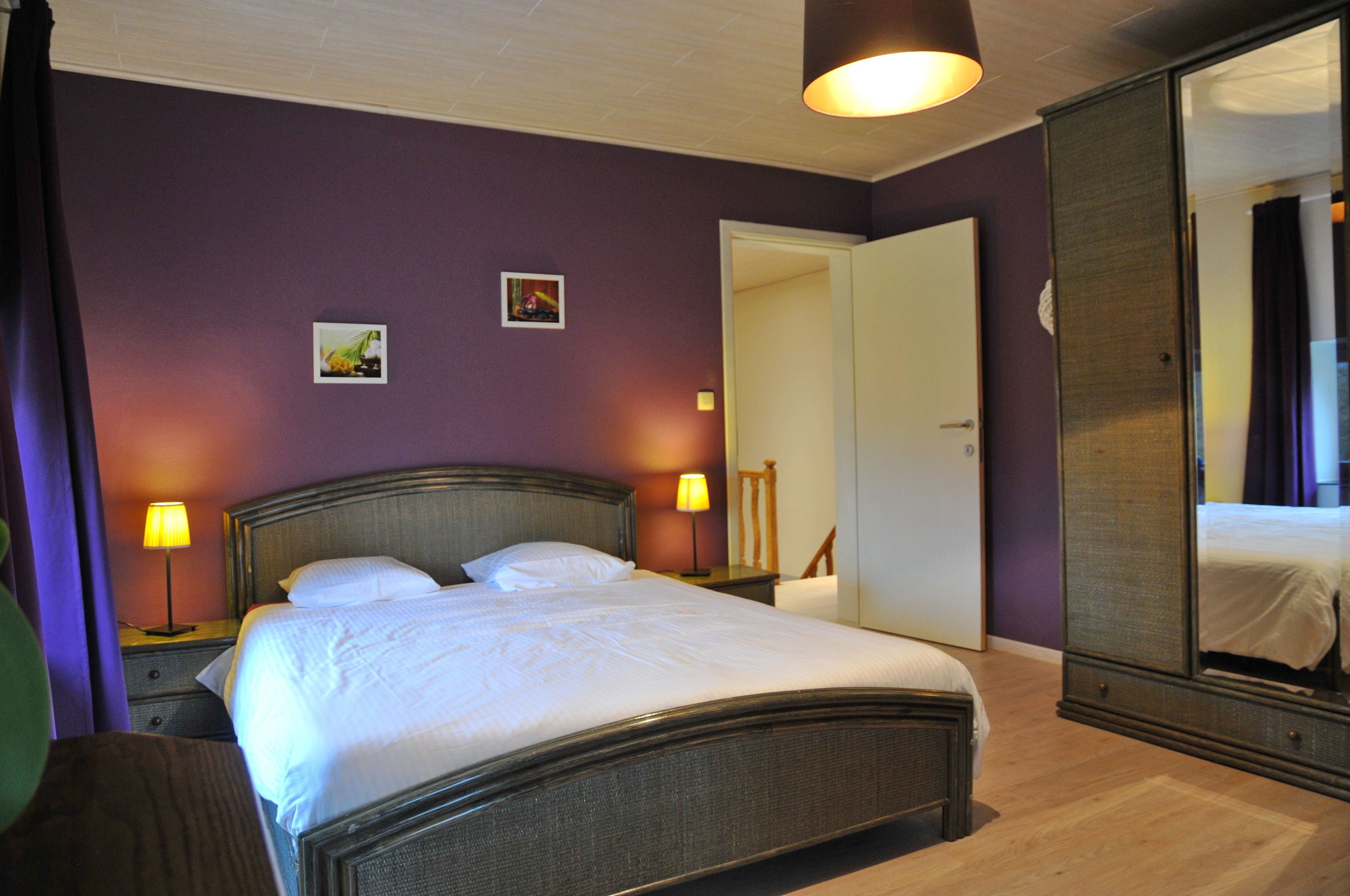 A well-lit bedroom with a large bed, two bedside lamps, and a wardrobe.