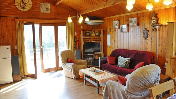 Interior de una cabaña de madera con un sofá, sillones, un televisor y un reloj en la pared.
